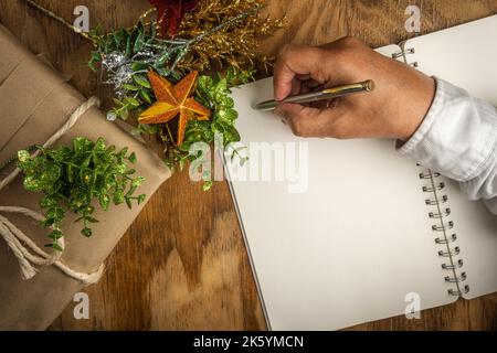 Christmas background of a man's hand writing a message in a notebook with a gift and decorations Stock Photo