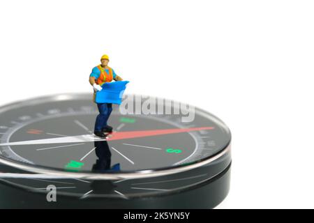 Miniature people toy figure photography. Project location concept. A construction worker with blueprint building standing with compass. Isolated on wh Stock Photo