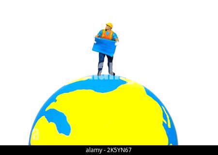 Miniature people toy figure photography. Project location concept. A construction worker holding blueprint standing above earth globe. Isolated on whi Stock Photo