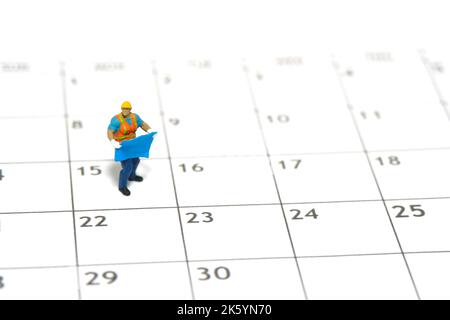 Miniature people toy figure photography. Project schedule time management concept. A construction worker holding blueprint standing above calendar. Is Stock Photo
