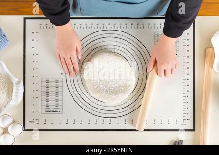 Top view of cooked wheat dough and hands of chef with rolling pin in hand on kitchen work surface Stock Photo