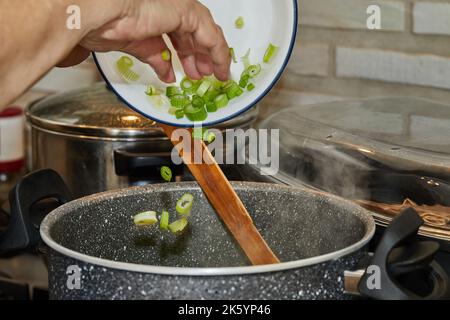Chef throws leek into pot on gas stove Stock Photo