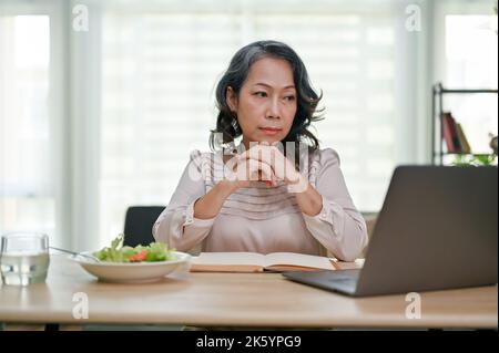 Professional and thoughtful aged-asian businesswoman or female executive manager working from home, concentrating on her new business strategy plan on Stock Photo