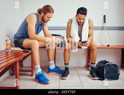 Two players using their cellphones together. Young squash players reading text messages on their smartphones together. Friends relaxing in a gym Stock Photo
