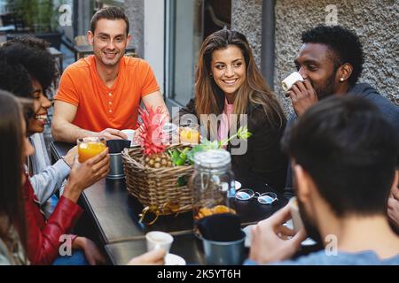 Group of young multiethnic young people at breakfast talking all together having fun at the brunch breakfast - diverse people at cafe drinking fruit j Stock Photo