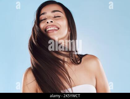 One beautiful young hispanic woman with healthy skin tossing her sleek long hair against a blue studio background. Happy mixed race model with Stock Photo