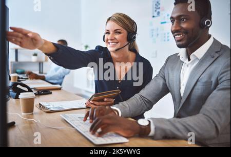 Happy caucasian female call centre telemarketing agent discussing plans with african american colleague while working together on computer in an Stock Photo