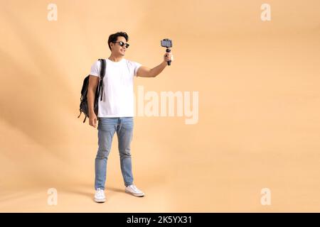 Young Asian tourist backpacker man smiling and taking a selfie and blog isolated on beige background Stock Photo