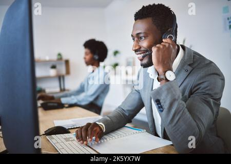 Happy young african american call centre telemarketing agent talking on a headset while working on computer in an office. Confident friendly male Stock Photo