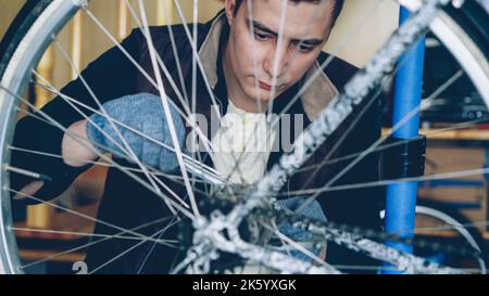Concentrated handsome guy skilled mechanic is repairing bicycle wheel with wrenchwhile working in his workplace. Bike maintenance, people and profession concept. Stock Photo