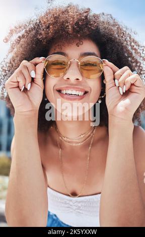 Portrait of young trendy beautiful mixed race woman with an afro smiling and posing alone outside. Hispanic woman wearing sunglasses and feeling happy Stock Photo