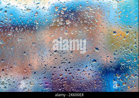 Drops Of Rain On Blue Glass Background. Street Bokeh Lights Out Of Focus. Autumn Abstract Backdrop. blurred outlines of buildings Stock Photo