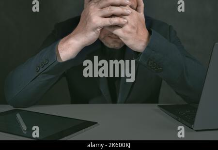 Tired businessman, frustrated with business failures and under stress, covers his face with his hands at his desk, workplace. desperate about losing m Stock Photo