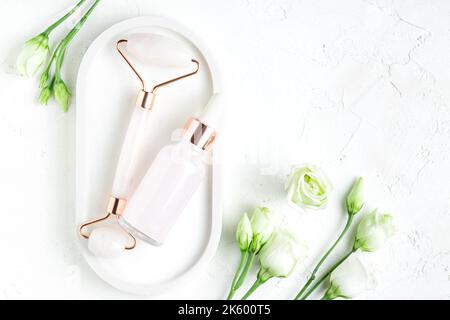 Beautiful composition of unbranded serum bottle, pink quartz stone face roller on white background. Anti-ageing cosmetics concept. Creative trendy cos Stock Photo