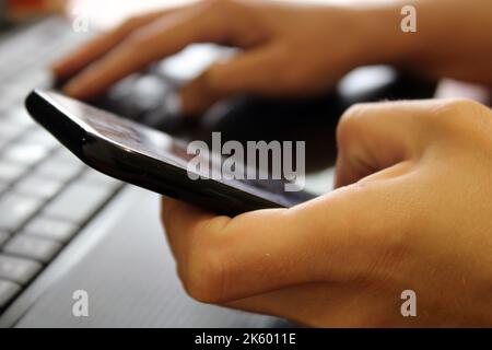 The girl sits at a laptop and holds a smartphone in her hands. Business concept. Online Shopping Stock Photo