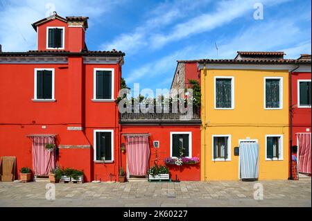 Bright red and yellow houses located against cloudy blue sky on sunny day on street of Burano Island in Italy Stock Photo