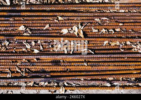 Top view old rusted iron bars and dry leaves on floor. Close up to stack of straight old rusty steel reinforcement structural steel bars from construc Stock Photo
