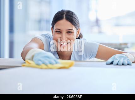 One beautiful smiling young mixed race woman cleaning the surfaces of her home. Happy Hispanic domestic worker wiping a table Stock Photo