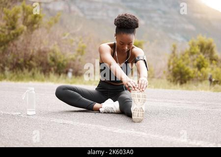 One african american female athlete with an afro listening to music on her earphones while exercising outdoors in nature. Dedicated black woman Stock Photo