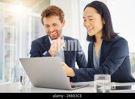 Two happy young diverse colleagues working together on a laptop in an office boardroom. Confident asian businesswoman explaining corporate plans and Stock Photo