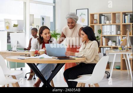 Diverse group of smiling business women using a laptop for a brainstorm meeting in an office. Happy confident professional team of colleagues using Stock Photo