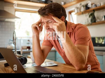 Young tired caucasian businessman suffering from a headache while working on a laptop from home alone. One stressed man looking unhappy while using a Stock Photo