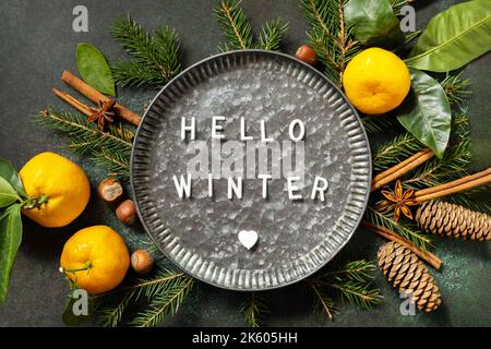 Hello winter text. Winter composition with fir branches, cones and tangerines. Cozy winter mood. Seasons greeting card. Stock Photo