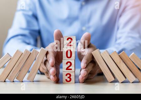 Businessman hand Stopping Falling of 2023 wooden Blocks. Business, Risk Management, Insurance, Resolution, strategy, solution, goal, New Year New You Stock Photo