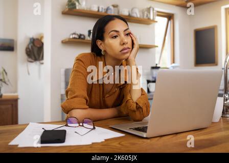 Bored mixed race businesswoman going through paper and bills and working on a laptop at home. Tired hispanic female businessperson thinking while Stock Photo