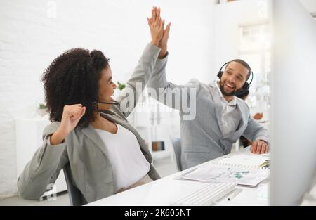 Two young happy mixed race call center agents giving each other a high five while answering calls in an office at work. Joyful hispanic customer Stock Photo