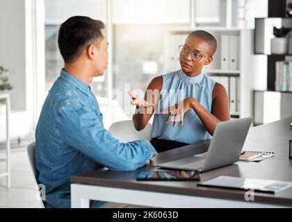 Two businesspeople having a meeting together in an office at work. Young african american businesswoman talking to an asian businessman. Colleagues Stock Photo
