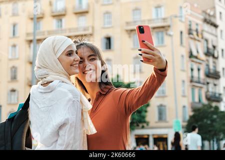 Young multiethnic female friends taking a selfie with a mobile phone outdoors on the street. Stock Photo