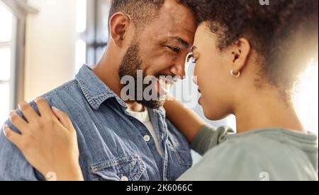 Young happy mixed race couple hugging while relaxing at home. Cozy hispanic husband and wife smiling while staring into each others eyes lovingly and Stock Photo