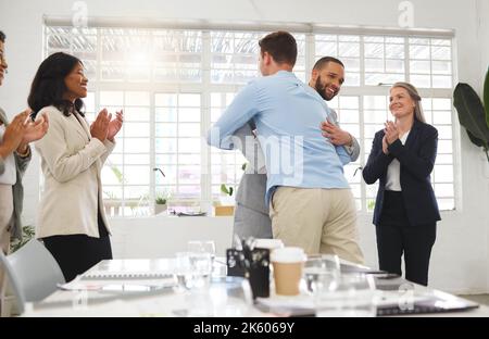 Businessmen hugging each other in support and unity while colleagues clap hands in a meeting at work. Diverse group of cheerful businesspeople Stock Photo