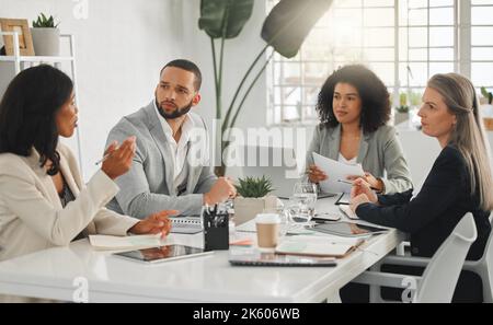 Group of four focused diverse businesspeople talking in a meeting together at work. Business professionals talking and planning in an office. Young Stock Photo