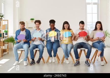 Group of happy diverse people sitting in row and holding colorful speech balloons Stock Photo