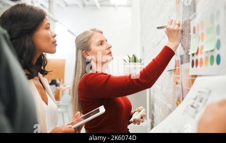Mature businesswoman brainstorming with staff. Leading businesswoman writing down her ideas. Serious businesswomen collaborate. Engineers working in Stock Photo