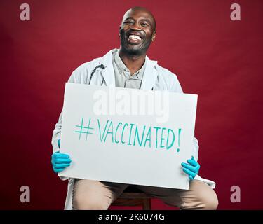 African american covid doctor holding and showing poster. Portrait of smiling black physician isolated on red studio background with copyspace. Man Stock Photo