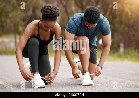 Fit african american couple tying their laces outdoors before a run. Young athletic man and woman training to improve their cardio and endurance for a Stock Photo