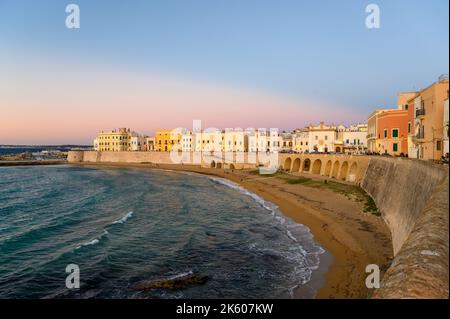 View across the bay and beach (Spiaggia della Purità) and waterfront facades of old town houses in evening sunlight in Gallipoli, Apulia, Italy. Stock Photo