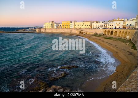 View across the bay and beach (Spiaggia della Purità) and waterfront facades of old town houses in evening sunlight in Gallipoli, Apulia, Italy. Stock Photo