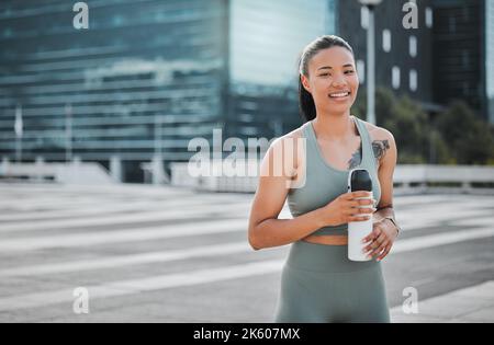 Young mixed race fit female athlete smiling and looking happy while taking a break resting drinking water and working out outside in the city Stock Photo