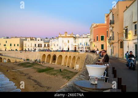 View across the bay and beach (Spiaggia della Purità) and waterfront facades of old town houses in evening sunlight in Gallipoli, Apulia, Italy. Stock Photo