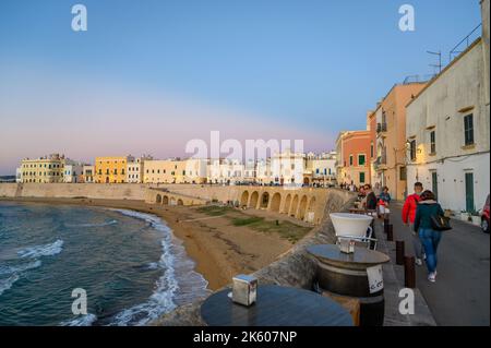 View across the bay and beach (Spiaggia della Purità) and waterfront facades of old town houses in evening sunlight in Gallipoli, Apulia, Italy. Stock Photo