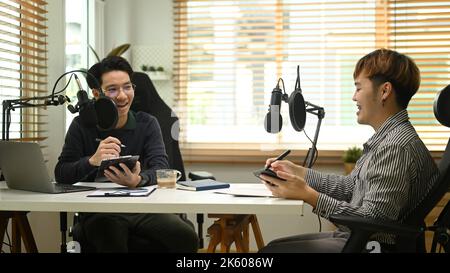 Two happy podcasters using condenser microphone, recording podcast from home studio. Radio, podcasts and technology concept Stock Photo