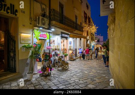 Tourists and locals walking along a typical narrow and cobbled street in old town Gallipoli in the evening, Apulia (Puglia), Italy. Stock Photo