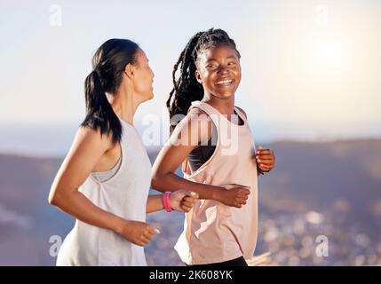 Two happy young female athletes smiling and talking while out for a run on a mountain road on a sunny day. Energetic young women running outdoors to Stock Photo
