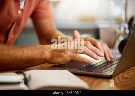 Man typing on a laptop while working from home alone. One businessperson working on a laptop and writing in a notebook while sitting at a table in the Stock Photo