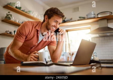 Young caucasian businessman on a call using a cellphone while working on a laptop and drinking coffee at home alone. Happy male businessperson smiling Stock Photo