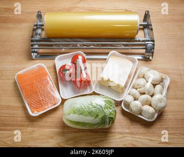 Tomatoes, mushrooms, cheese, salmon fillets and Chinese cabbage are wrapped in cling film for better storage. Roll of transparent food film for packin Stock Photo